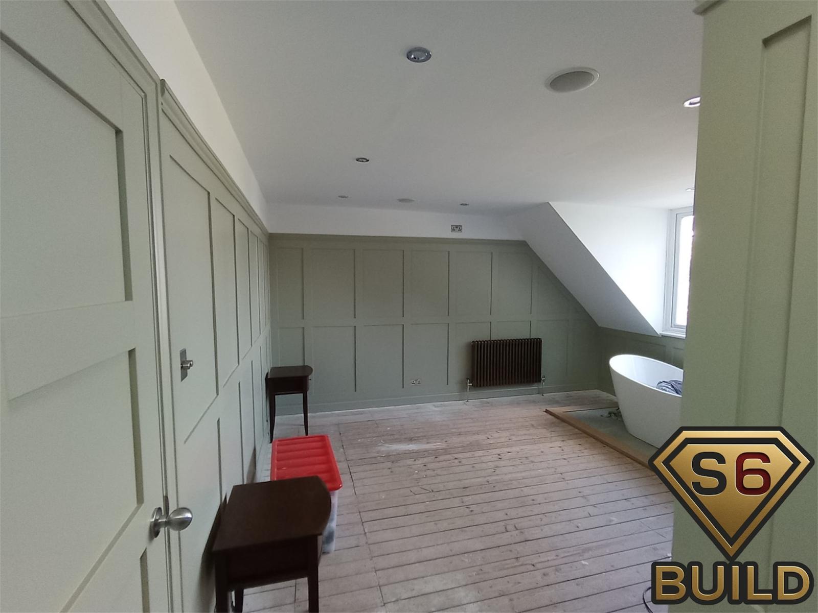 Sage green wall panelling and fitted doors in a loft bathroom